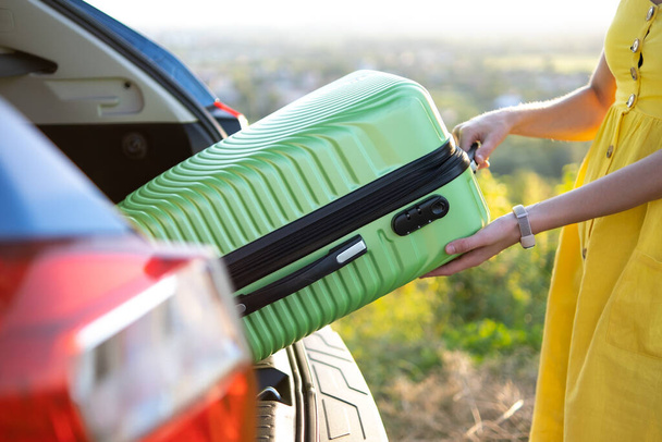 Primer plano de la mujer que toma la maleta verde del maletero del coche. Concepto de viajes y vacaciones - Foto, imagen