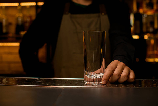 vista frontal de vidrio de cóctel transparente limpio y vacío en el mostrador de bar que sostiene la mano masculina - Foto, Imagen