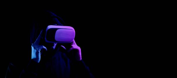 Sanal gerçeklik oyunu. Sanal gerçeklik teknolojisi için dijital gözlüklü genç adam karanlık neon arka planda izole edildi. 3 boyutlu simülasyonda çalışma ve sanal dünya - Fotoğraf, Görsel