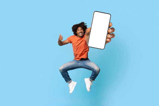 Chico negro divertido con el pelo tupido que muestra el teléfono móvil, maqueta - Foto, Imagen