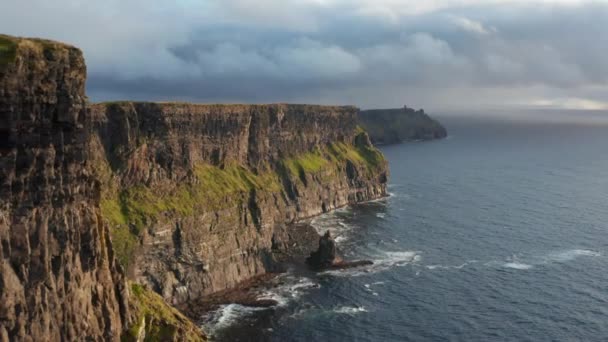 Krásné panoramatické záběry dlouhých a vysokých útesů na mořském pobřeží. Zpětně létají po rozeklané skalní stěně nad vlnitou vodní hladinou. Útesy Moher, Irsko - Záběry, video