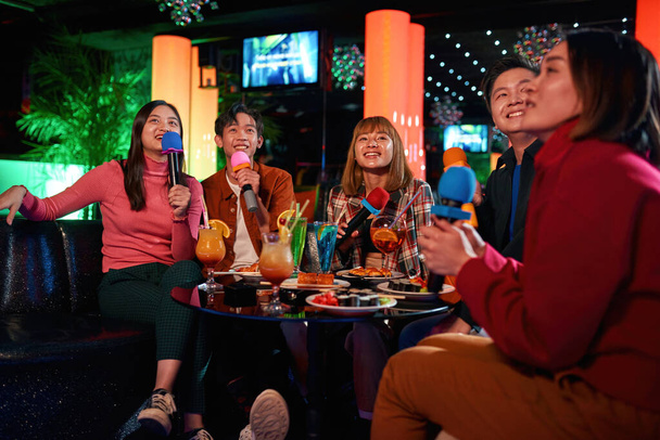 Cheerful asian friends laughing and singing songs at karaoke club - Foto, afbeelding