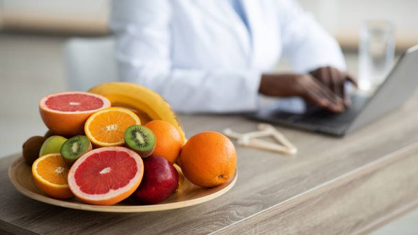 Biurko dietetyczne ze zdrowymi owocami i zaciskiem, dietetyk pracujący na laptopie, siedzący w miejscu pracy, wybiórcze skupienie - Zdjęcie, obraz