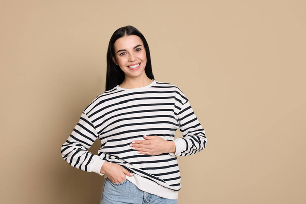 Happy healthy woman touching her belly on beige background - Photo, image
