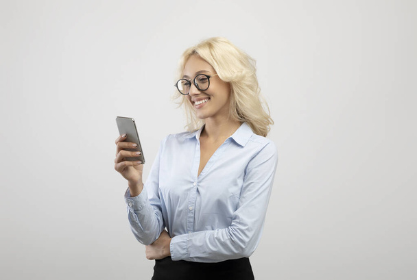 Portrait of young female entrepreneur with cellphone working online or chatting with client over light studio background - Foto, Imagem