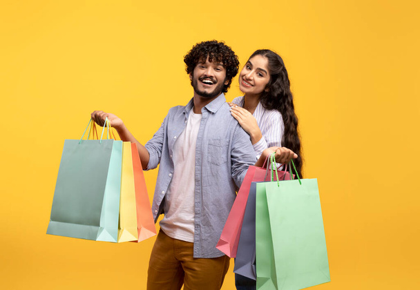 Concepto de ventas estacionales. Feliz joven pareja india sosteniendo paquetes de colores en las manos, y sonriendo a la cámara - Foto, imagen