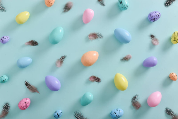 Colored eggs in pastel tones and feathers on a light blue background. The minimum composition of Easter. A holiday card with eggs. copy space - Foto, Imagem
