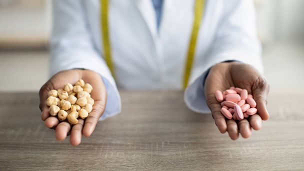 Zdravá výživa vs léky koncept. Ženské dietní drží tablety a ořechy u stolu na klinice, detailní pohled - Fotografie, Obrázek