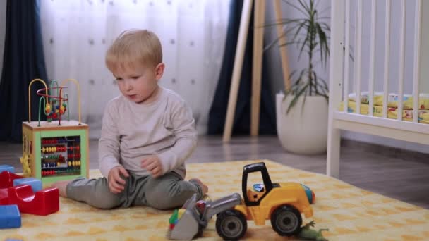 счастливый ребенок играет с игрушечной машиной, сидя на полу в детской комнате - Кадры, видео