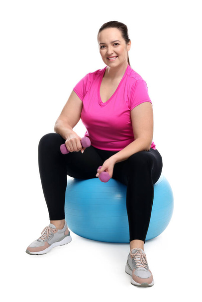 Happy overweight woman with dumbbells sitting on fitness ball against white background - Photo, image