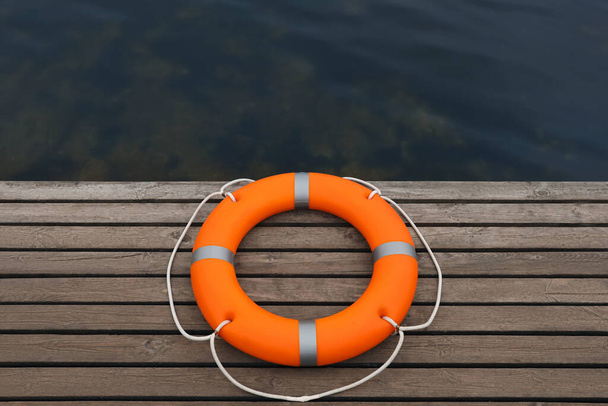 Orange lifebuoy on wooden pier near water. Rescue equipment - Foto, Imagem