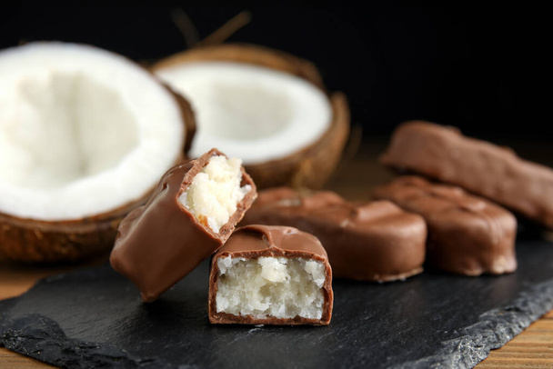 Delicious milk chocolate candy bars with coconut filling on slate plate, closeup - Photo, Image