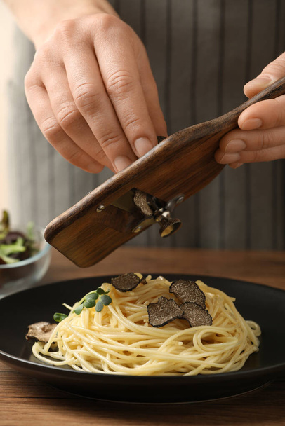 Woman slicing truffle onto spaghetti at wooden table, closeup - Photo, image