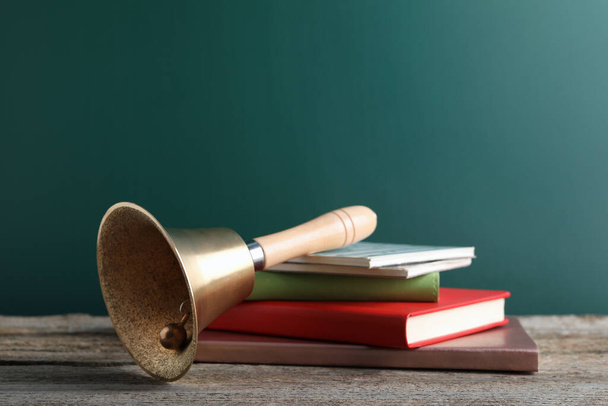 Golden bell and books on wooden table near green chalkboard. School days - Foto, imagen