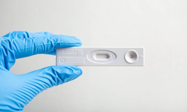 Doctor in gloves holding disposable express test for hepatitis on white background, closeup - 写真・画像