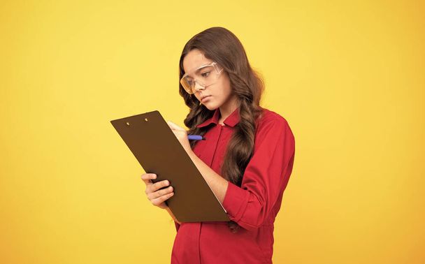 Konzentriertes Teenager-Mädchen mit Schutzbrille, das Notizen in einem Ordner mit Dokumenten macht, Studie - Foto, Bild