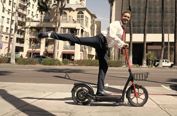 szczęśliwy człowiek biznesmen jazda elektro skuter na tle miasta krajobraz, wynajem transportu. - Zdjęcie, obraz