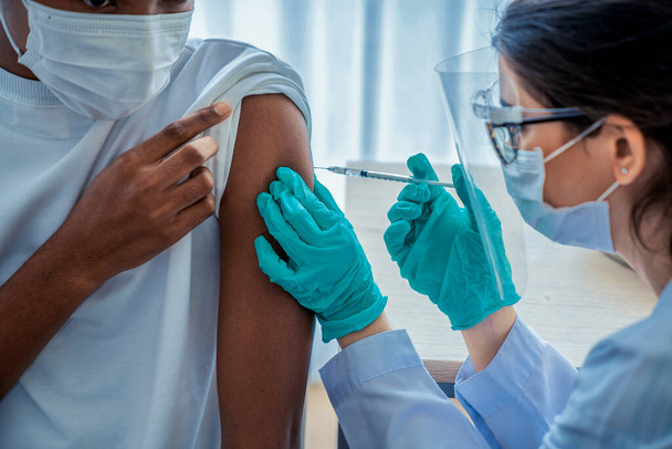 Νεαρός επισκέπτεται επιδέξιο γιατρό στο νοσοκομείο για εμβολιασμό - Φωτογραφία, εικόνα
