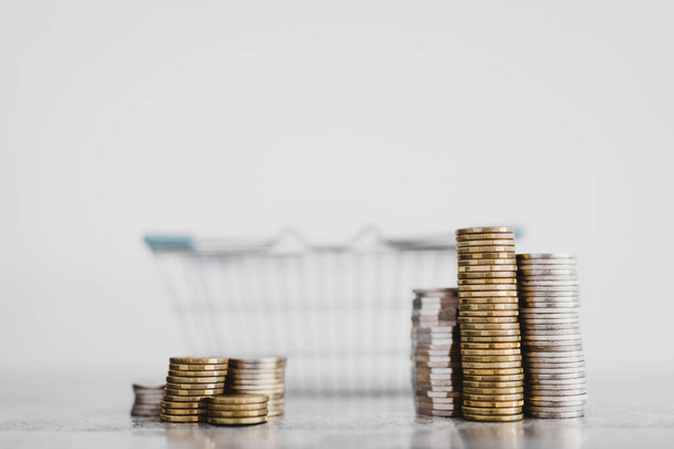 stacks of different coins inside of shopping basket on white background shot at shallow depth of field with minimalist composition, concept of expenses and consumer behaviour  - Φωτογραφία, εικόνα