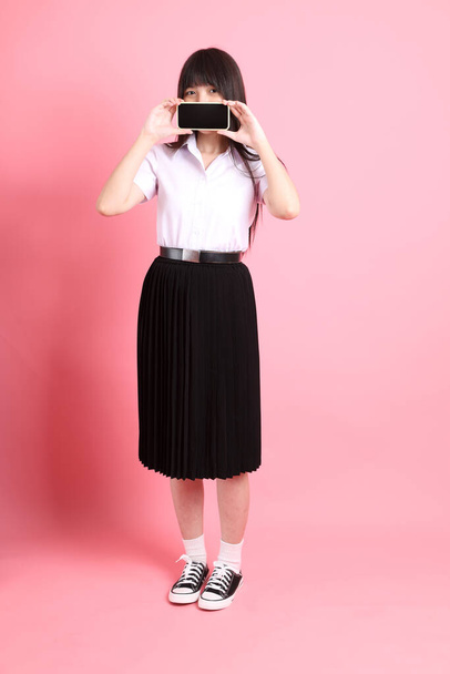 La chica asiática adolescente con uniforme universitario de pie sobre el fondo rosa. - Foto, imagen