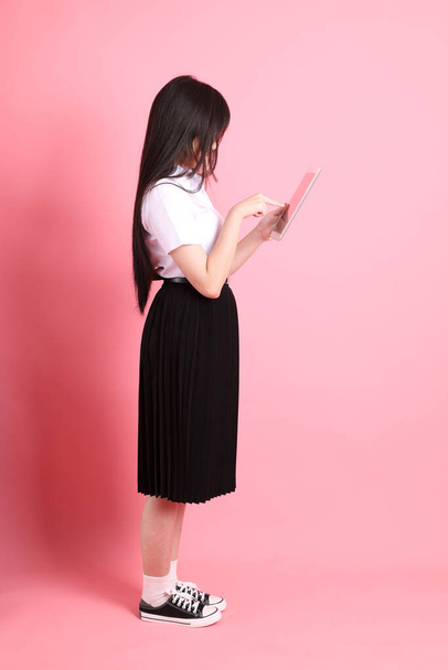 de tiener aziatische meisje met universiteit uniform staan op de roze achtergrond. - Foto, afbeelding