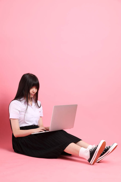 La chica asiática adolescente con uniforme universitario sentado en el fondo rosa. - Foto, Imagen