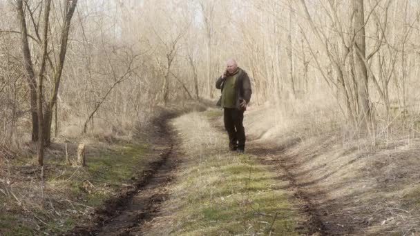  un hombre con un portátil bajo su brazo emocionalmente gesticulante hablando en un teléfono móvil en el bosque - Metraje, vídeo