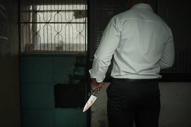 Ένας εγκληματίας επιχειρηματίας που φοράει ένα λευκό μακρυμάνικο πουκάμισο κρατώντας ένα ματωμένο μαχαίρι επιτίθεται βάναυσα στο θύμα του σε ένα δωμάτιο, υπάρχει χώρος για κείμενο, Έννοια Ποινικού, Εγκλήματος, Δολοφονίας. - Φωτογραφία, εικόνα
