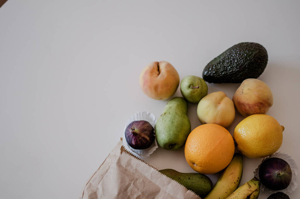 Una variedad de frutas en una bolsa de papel hecha a mano se encuentran en la mesa. Piso saludable yacía con espacio de copia. Aguacates, limones, melocotones, peras, naranjas. - Foto, Imagen