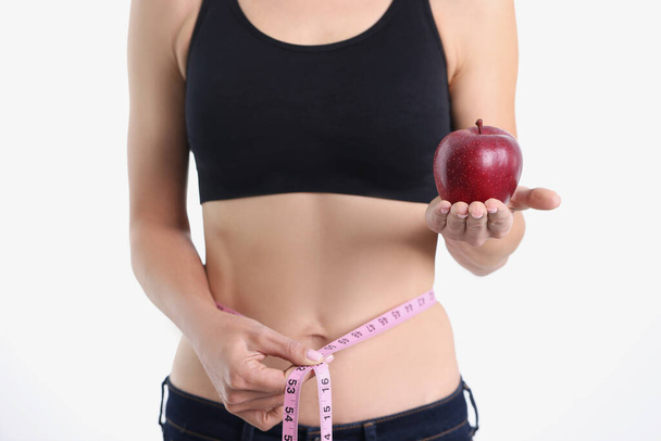 Slender girl shows apple and measuring tape around waist - Fotoğraf, Görsel