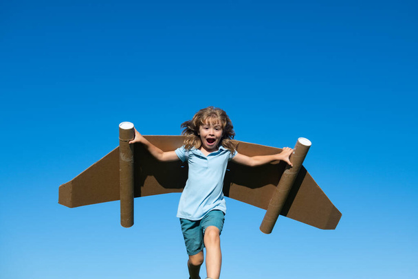 Kid with jet pack superhero. Child pilot against summer sky background. Boy with paper plane flight, toy airplane with cardboard wings, Imagination, kids freedom. - Foto, imagen
