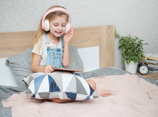 Aranyos kislány fülhallgatóban tabletet használ otthon. - Fotó, kép