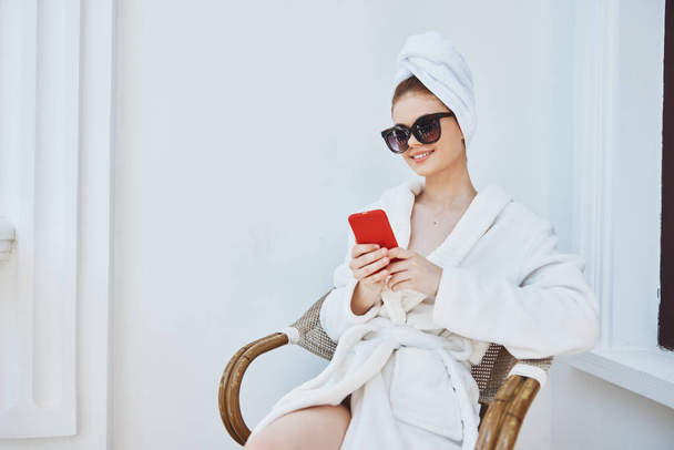 kobieta w okularach przeciwsłonecznych z telefonem na balkonie w godzinach porannych. Wysokiej jakości zdjęcie - Zdjęcie, obraz