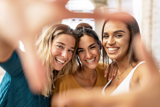 Drie multiraciale vrouwelijke vrienden nemen selfie en het maken van hand frame gebaar in de straat, kijken door vingers naar de camera - Diverse jonge vrouwen plezier hebben op vakantie - Millennial people concept - Foto, afbeelding