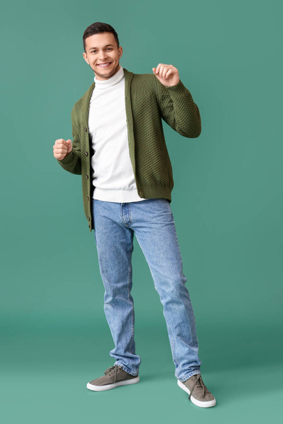 Young man in jumper dancing on green background - Фото, изображение