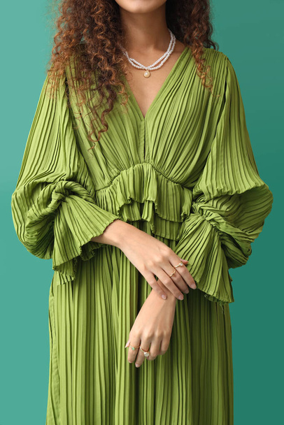 Jonge vrouw in jurk met stijlvolle sieraden op groene achtergrond - Foto, afbeelding