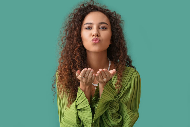 Young African-American woman in dress with jewelry blowing kiss on green background - Fotografie, Obrázek