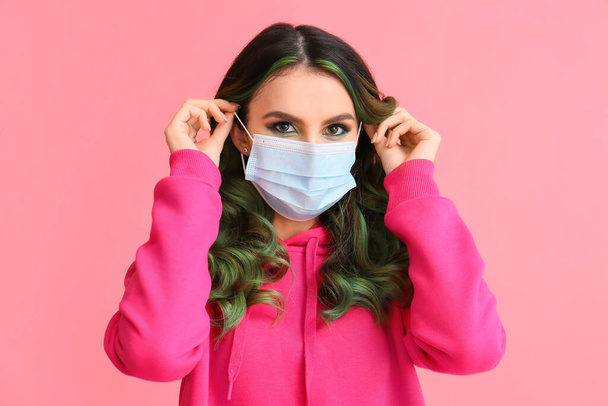 Beautiful young woman with unusual green hair wearing medical mask on color background - Photo, Image