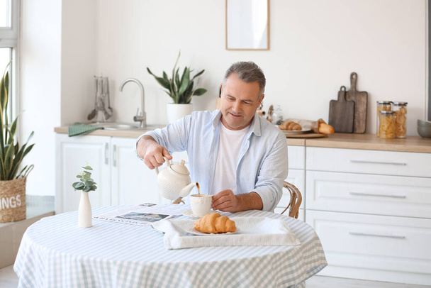 シニア男puring茶にカップでテーブルでキッチン - 写真・画像