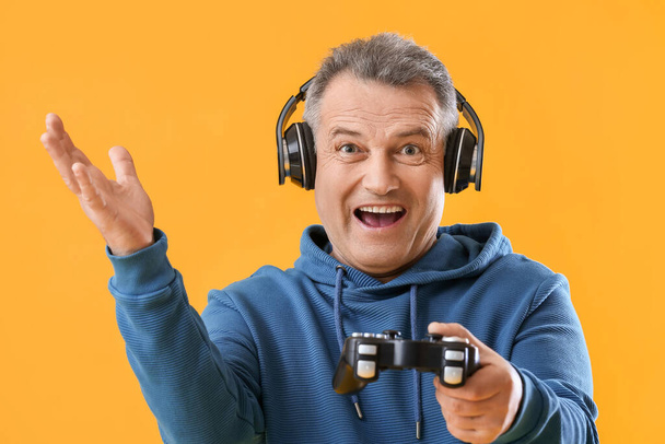 Šťastný senior muž ve sluchátkách s herní podložkou na žlutém pozadí - Fotografie, Obrázek