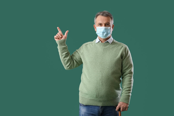 Starší muž v lékařské masce ukazuje na něco na zeleném pozadí - Fotografie, Obrázek