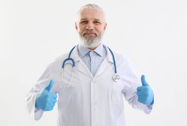 Зрелый врач-мужчина со стетоскопом показывает большой палец вверх на белом фоне - Фото, изображение