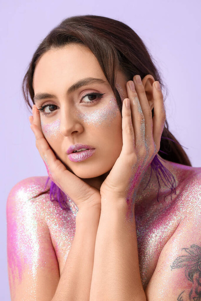 Beautiful young woman with glitters on her face and body against color background - Valokuva, kuva