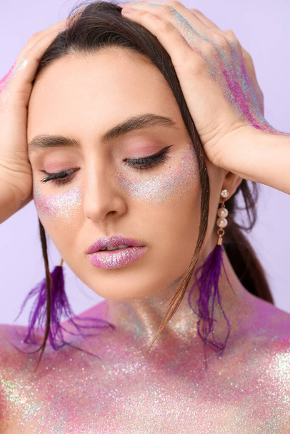 Beautiful young woman with glitters on her face and body against color background - Photo, Image