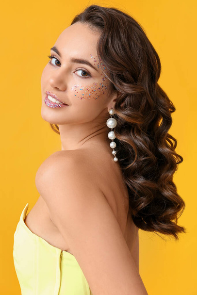 Красивая молодая женщина с блестками на лице на желтом фоне - Фото, изображение