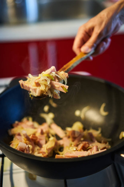 Pork ham, onions and herbs stir frying in a wok on the gas stove - Fotó, kép