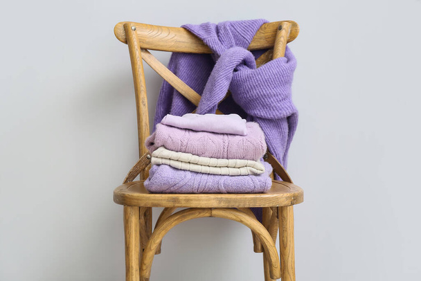 Cadeira de madeira com camisolas de malha perto da parede clara - Foto, Imagem
