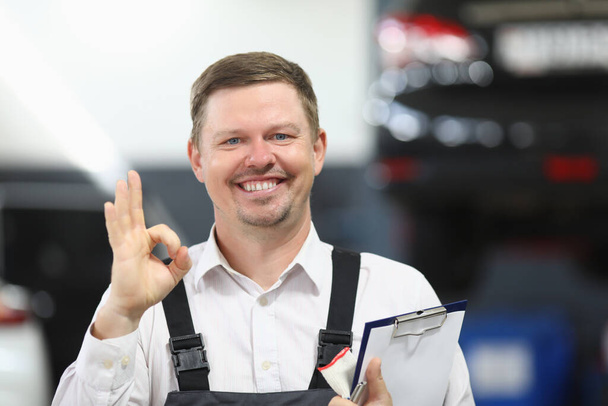 Garage service medewerker vertonen ok teken met de hand en gelukkig glimlachen in uniform - Foto, afbeelding