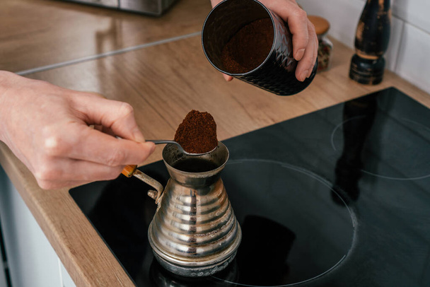Close up de mãos de homem irreconhecível colocando colher de chá cheio amontoado de café moído de lata redonda em cezve de cobre. - Foto, Imagem