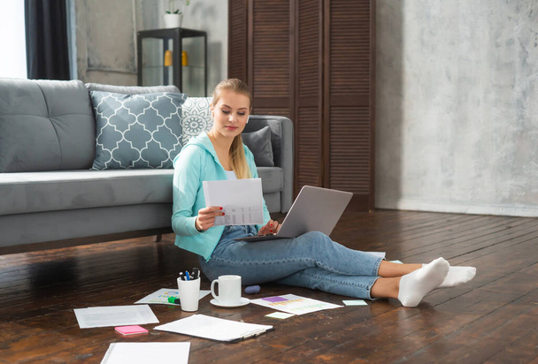 若い女性は自宅の床に座っている間、ノートパソコンを使用して文書で動作します。学生、起業家やフリーランスの女の子は、インターネットを介してリモートで仕事や勉強. - 写真・画像